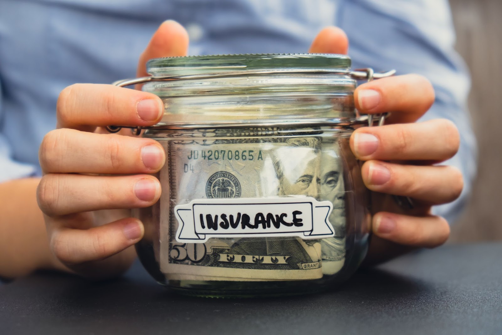 Person holding a jar with money in it with the word “insurance” on the cover. 