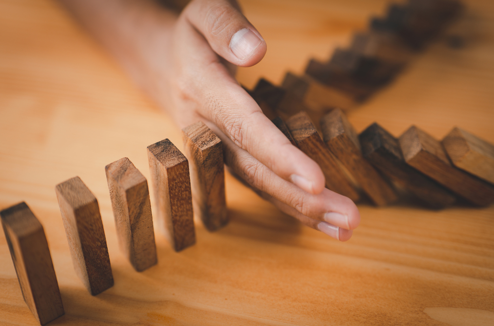 Photo of a man's hand preventing fallen wooden dominoes from knocking over more dominoes.