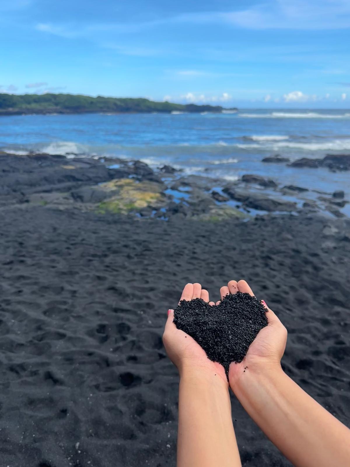 A person holding black sand in their hands

Description automatically generated