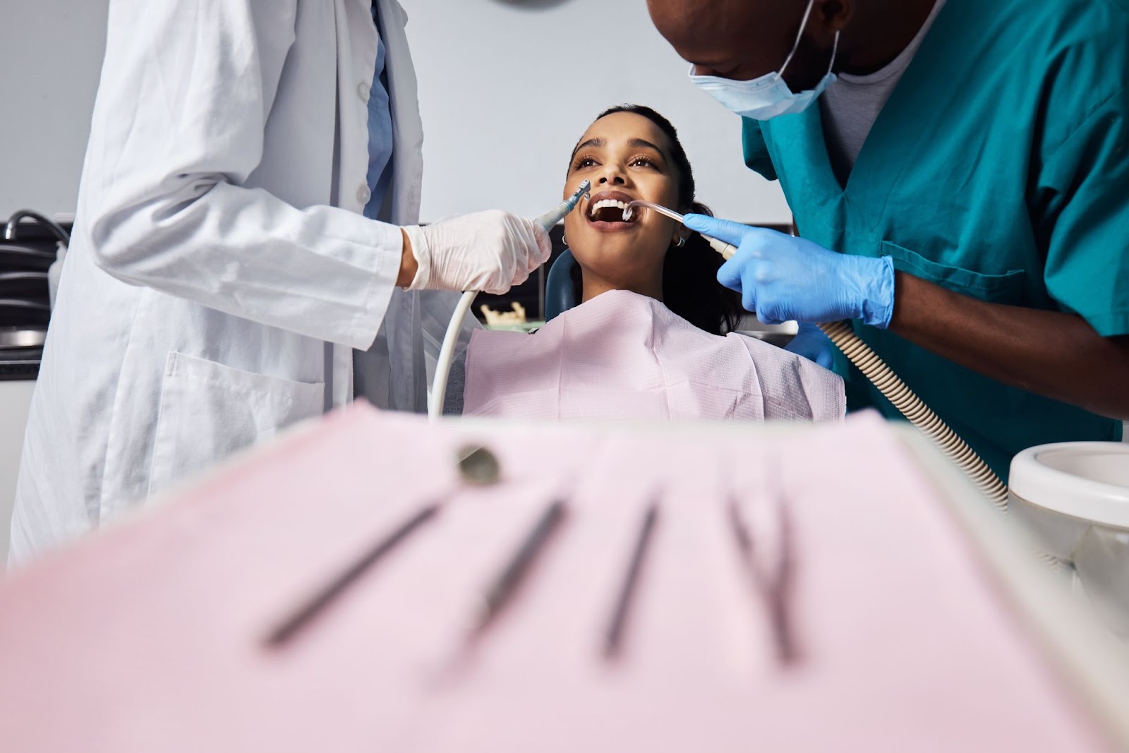 A young woman enjoying pain-free dental care. The dentist and assistant work on her teeth, with dental tools neatly arranged on a tray in the foreground.