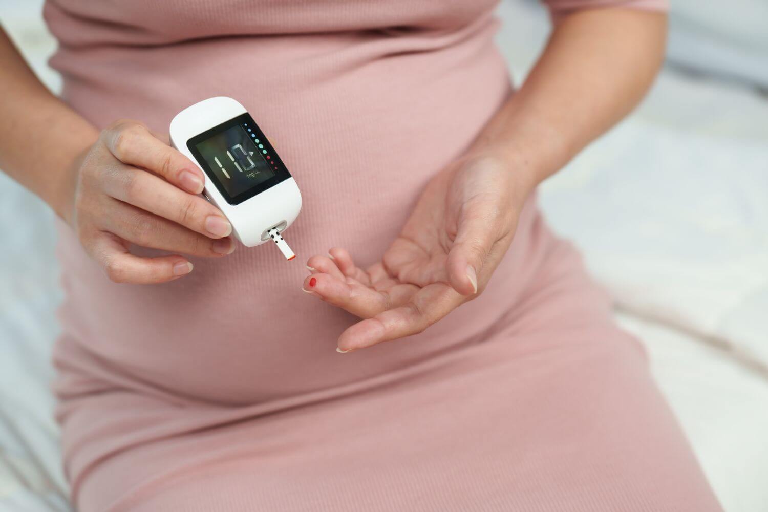 Pregnant woman holding glucose meter to check blood sugar at home