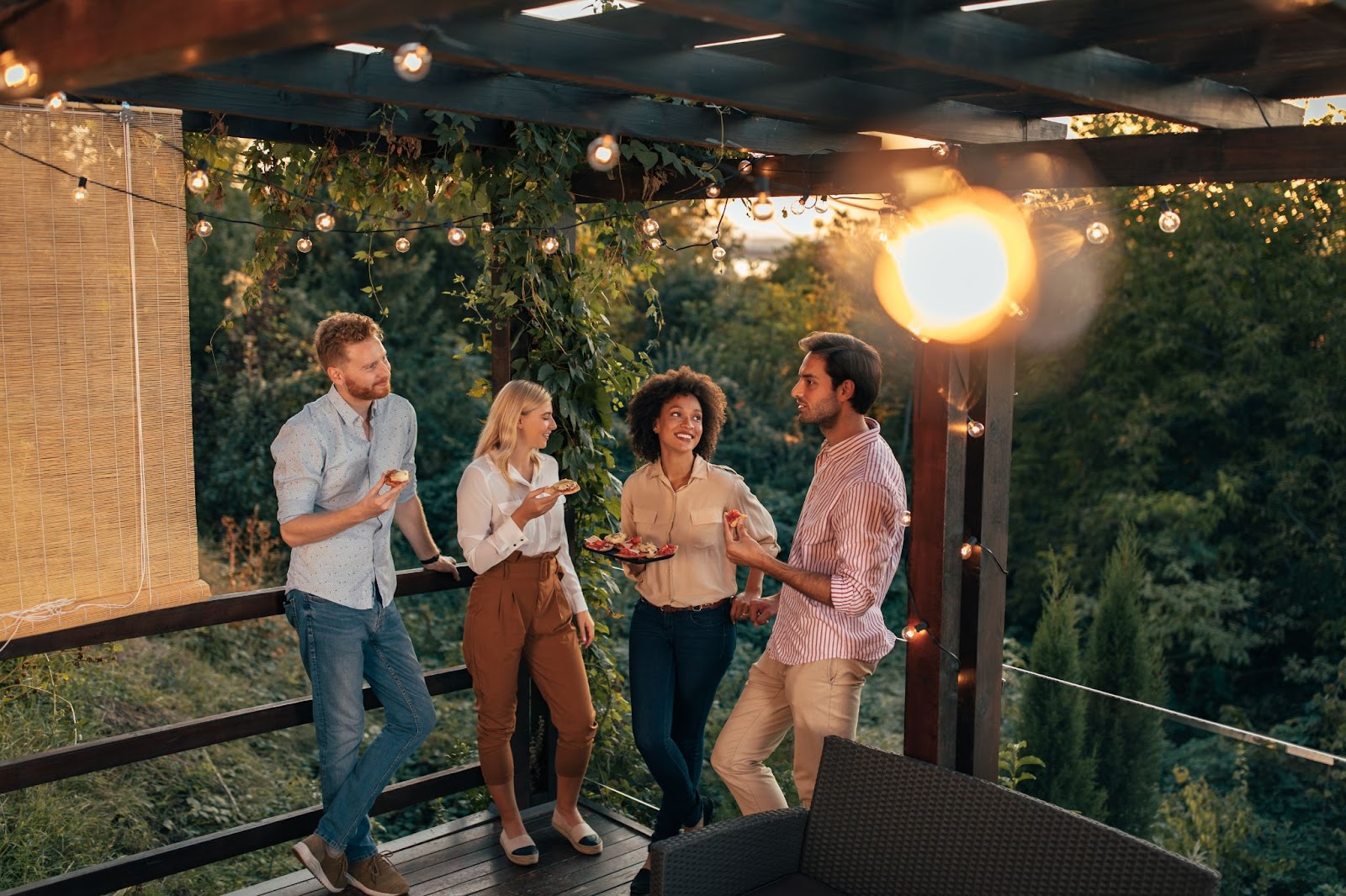 Four friends are enjoying eating pizzas on a porch. 