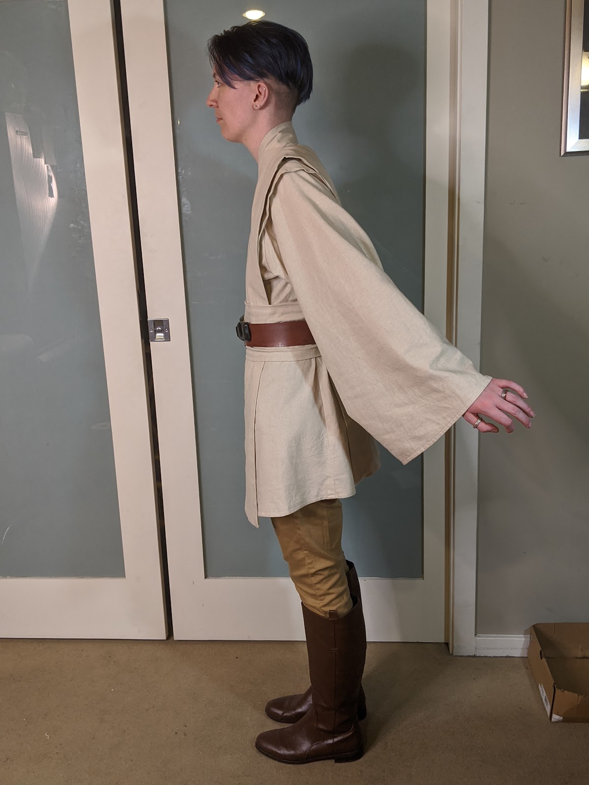 Image description: A person in a Jedi costume, facing towards the left, with their arms extended behind them. /end description