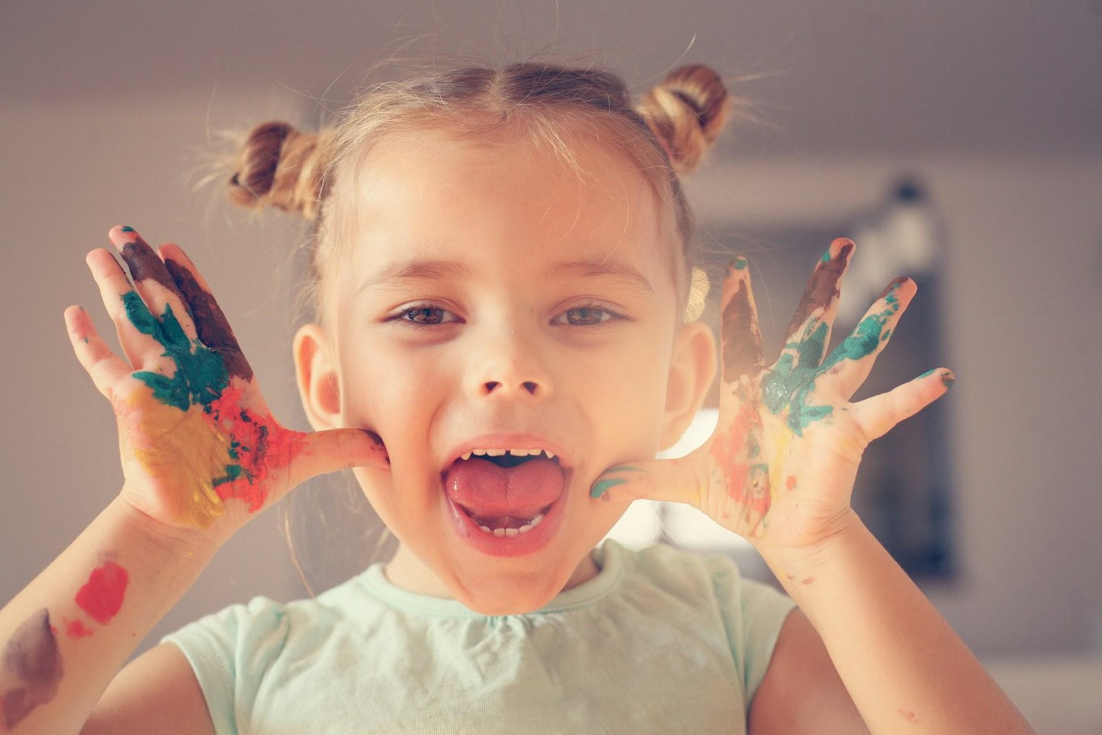 A girl smiling with paint all over her hands, pulling a funny face