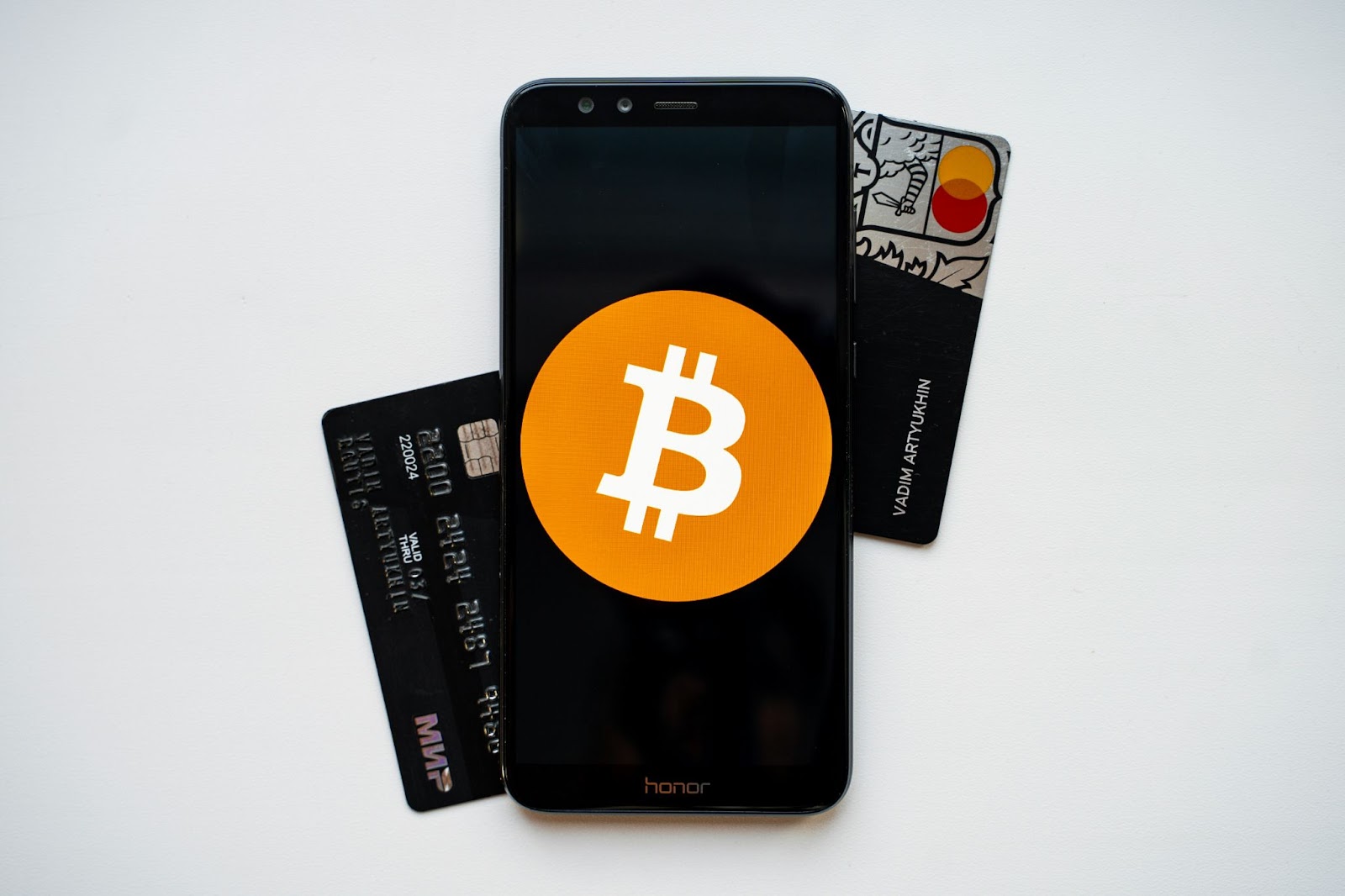 A smartphone displaying a Bitcoin symbol, flanked by two credit cards