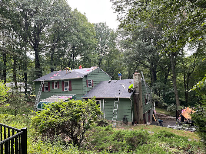 A team from Boundless Roofing & Chimney replacing the damaged roof of a house surrounded by trees and vegetation.