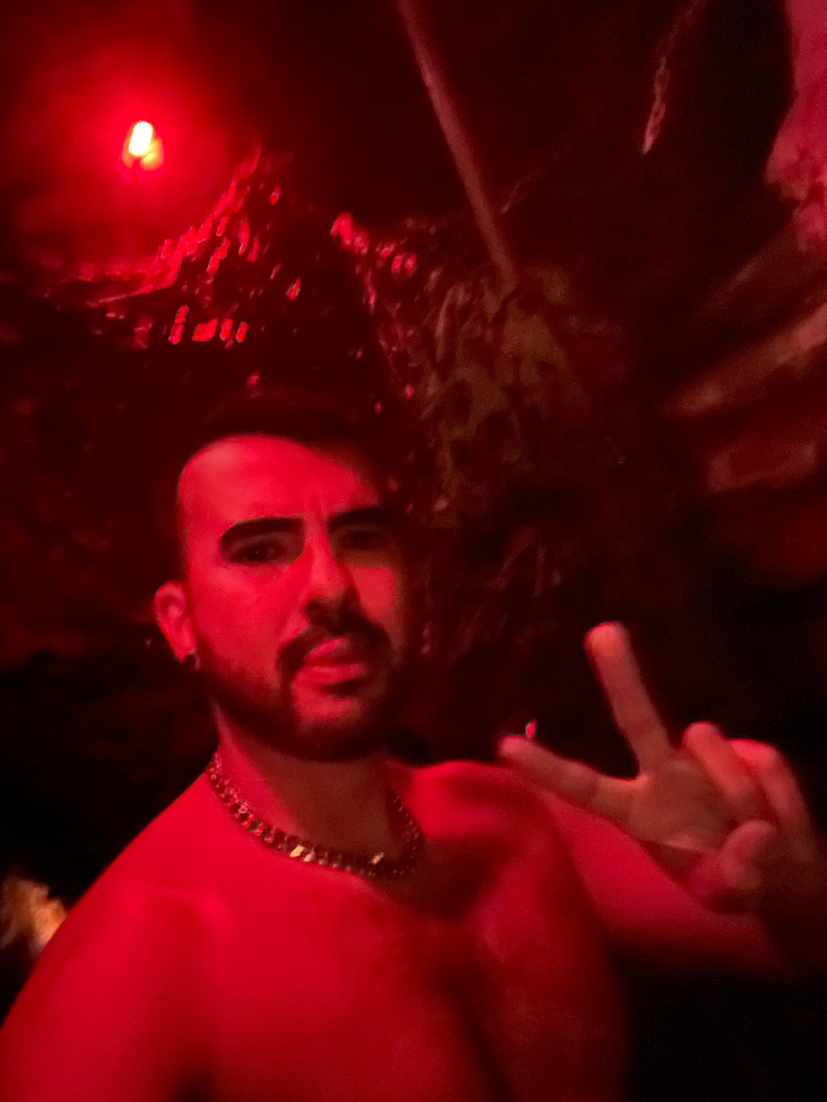gay xxx content creator and influencer phil flashes a peace sign shirtless in L’impact’s dungeon gay cruising bar in paris