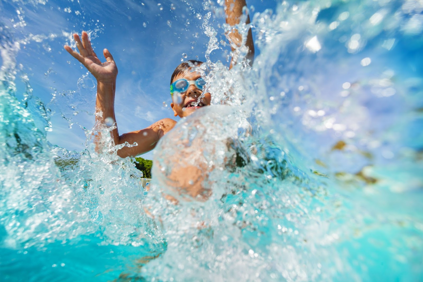 Criança com óculos de natação em uma piscina, jogando água para cima.