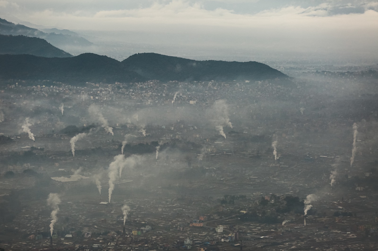 A dystopian view of Kathmandu valley skyline engulfed in thick smog and smoke. The air is heavy with pollution, obscuring buildings and mountains in the background. The image portrays a grim, post-apocalyptic atmosphere, highlighting the urgent need for environmental action