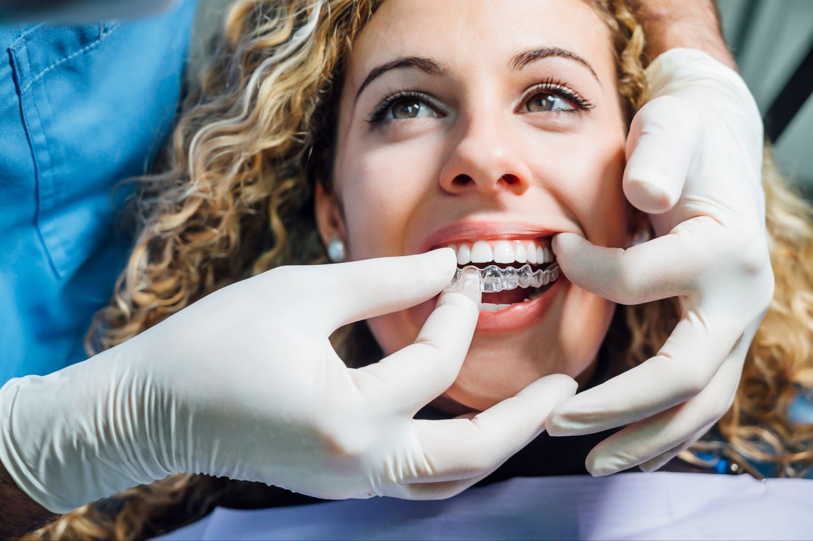 Close-up view of dentist wearing gloves fitting an Invisalign aligner in patient's smile.