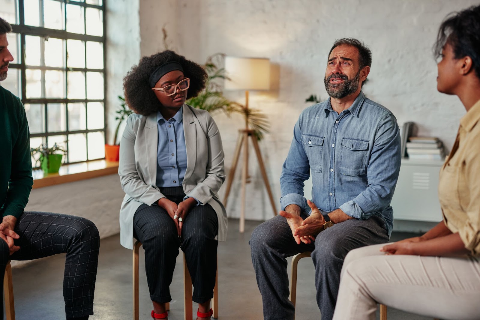 People sitting in a circle and talking with a window and lamp in the background. 