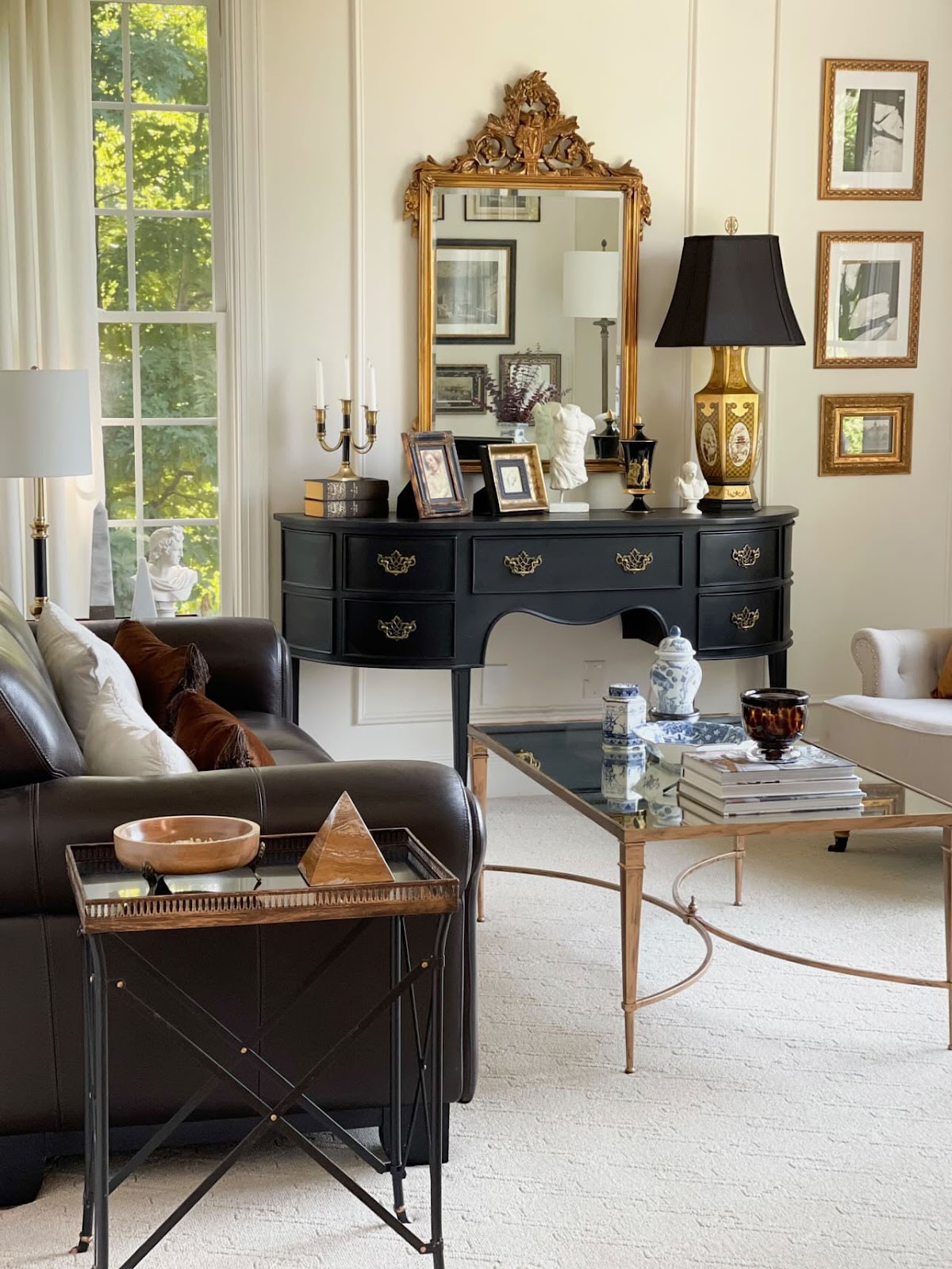 Ebonized server table with brass pulls in Nancy's living room. Displayed are framed photos, sculptures, candelabra, lamp, and mirror. Gilt artwork and furniture complete the elegant space.