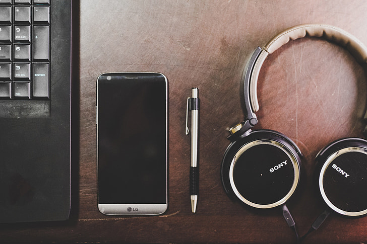 A smartphone, pen and a headphone alongside a laptop.
