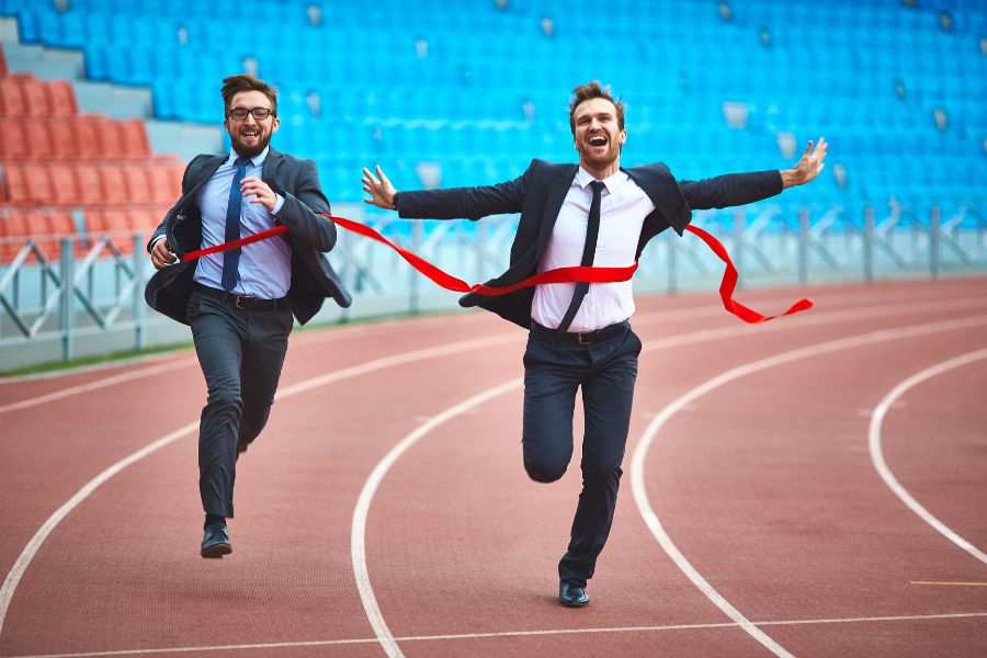 Two businessmen in suits racing, one crossing the finish line.