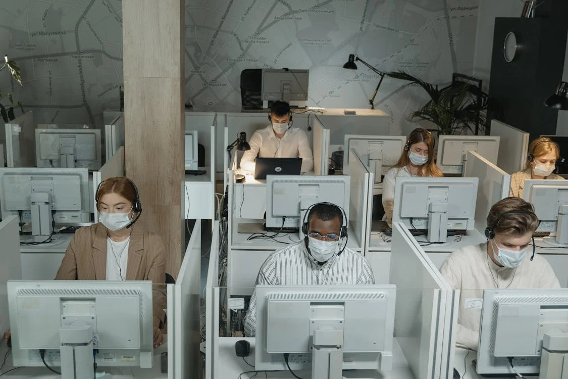 Office workers wearing masks, seated at desks with computers.