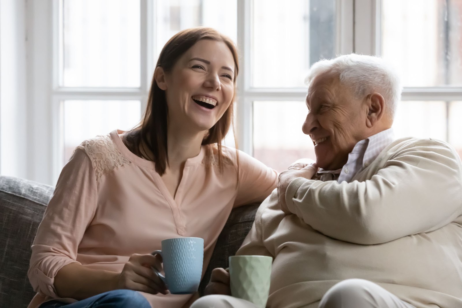 A senior man with dementia and his adult daughter laughing together over coffee.