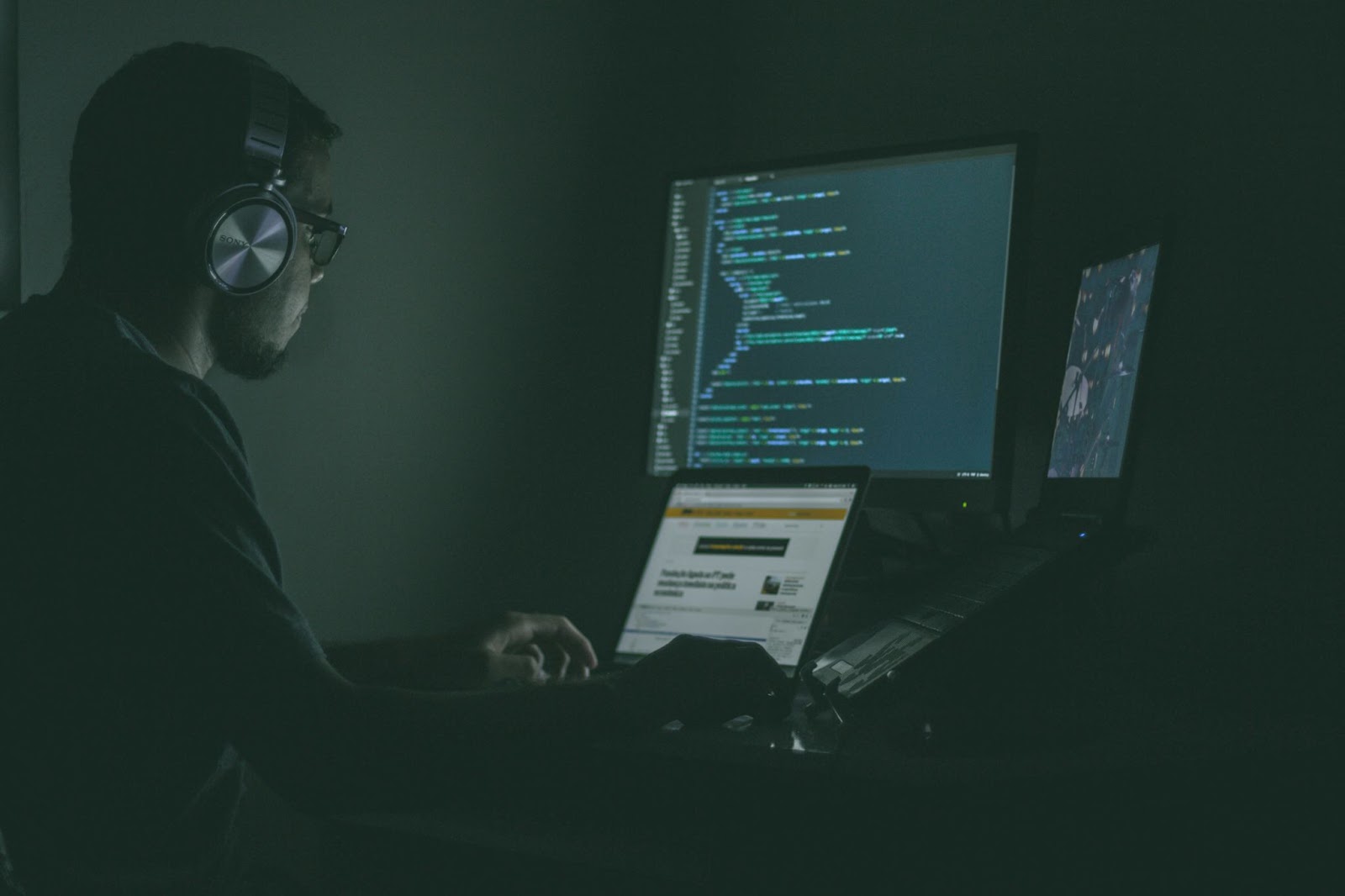 A programmer working in a dark environment with multiple computer screens