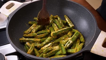Marinated bhindi being stir-fried in hot oil in the frying step of Bhindi Masala.