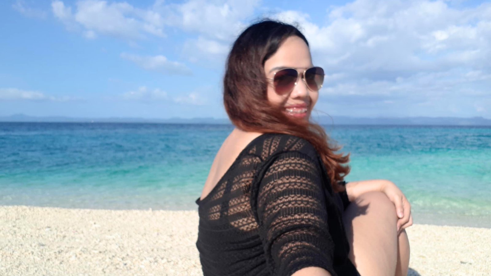 A lady tourist sitting on the beach with the Pacific Ocean as her backdrop.