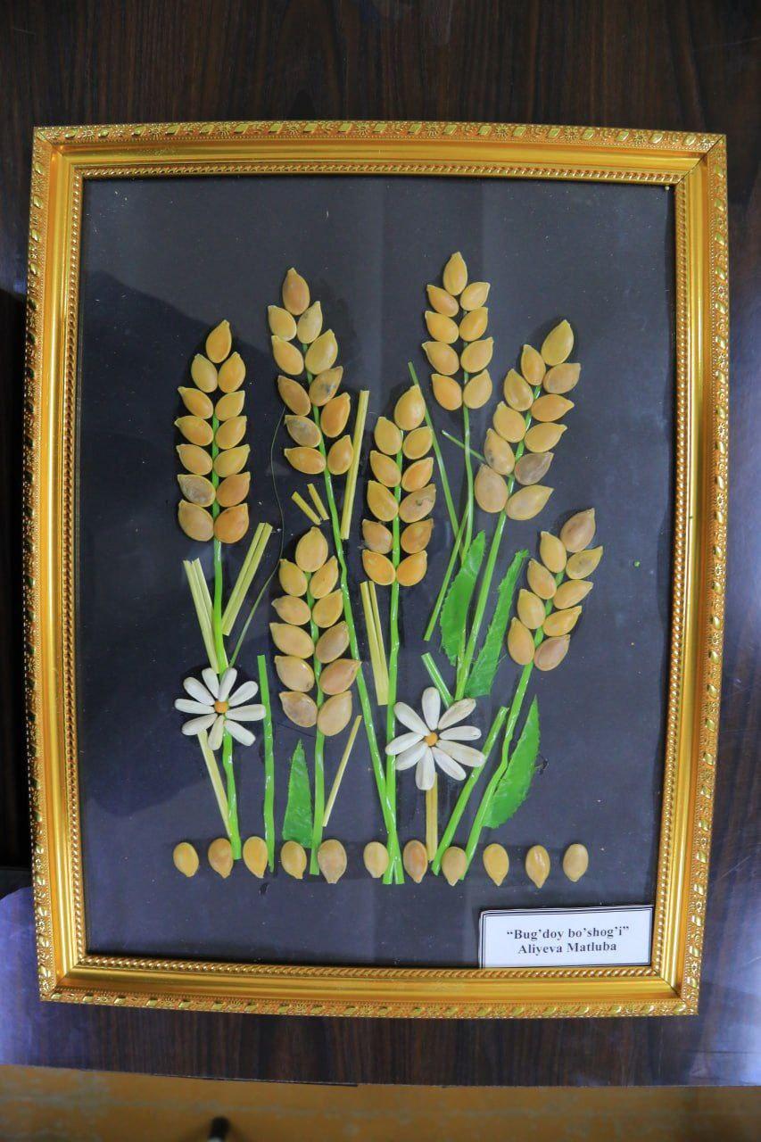 Mosaic art of wheat plants on green stalks with white flowers with yellow centers, made from seeds and blades of grass. 