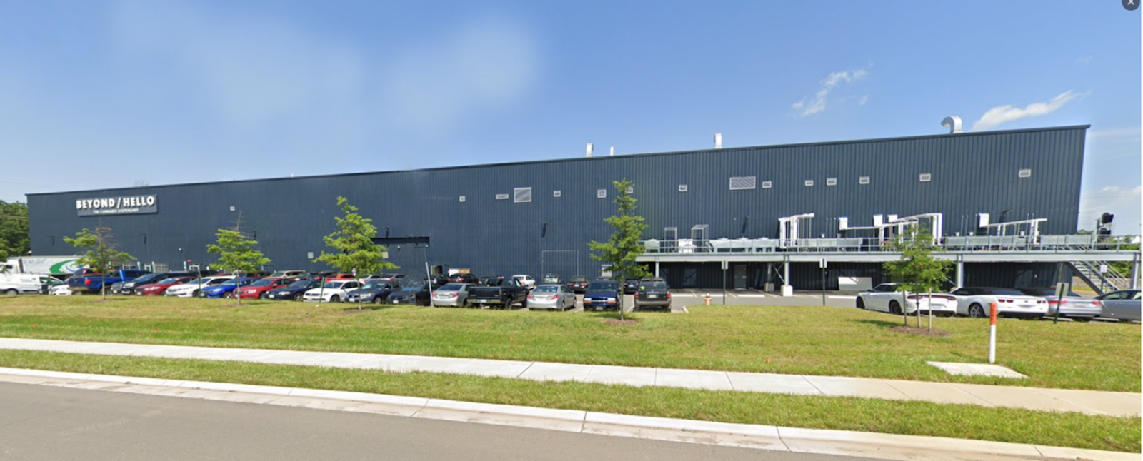 The completed pre-engineered steel factory building called Dalitso Cannabis Processing Facility with a parking lot full of cars and some landscaping including trees and grass in the foreground.