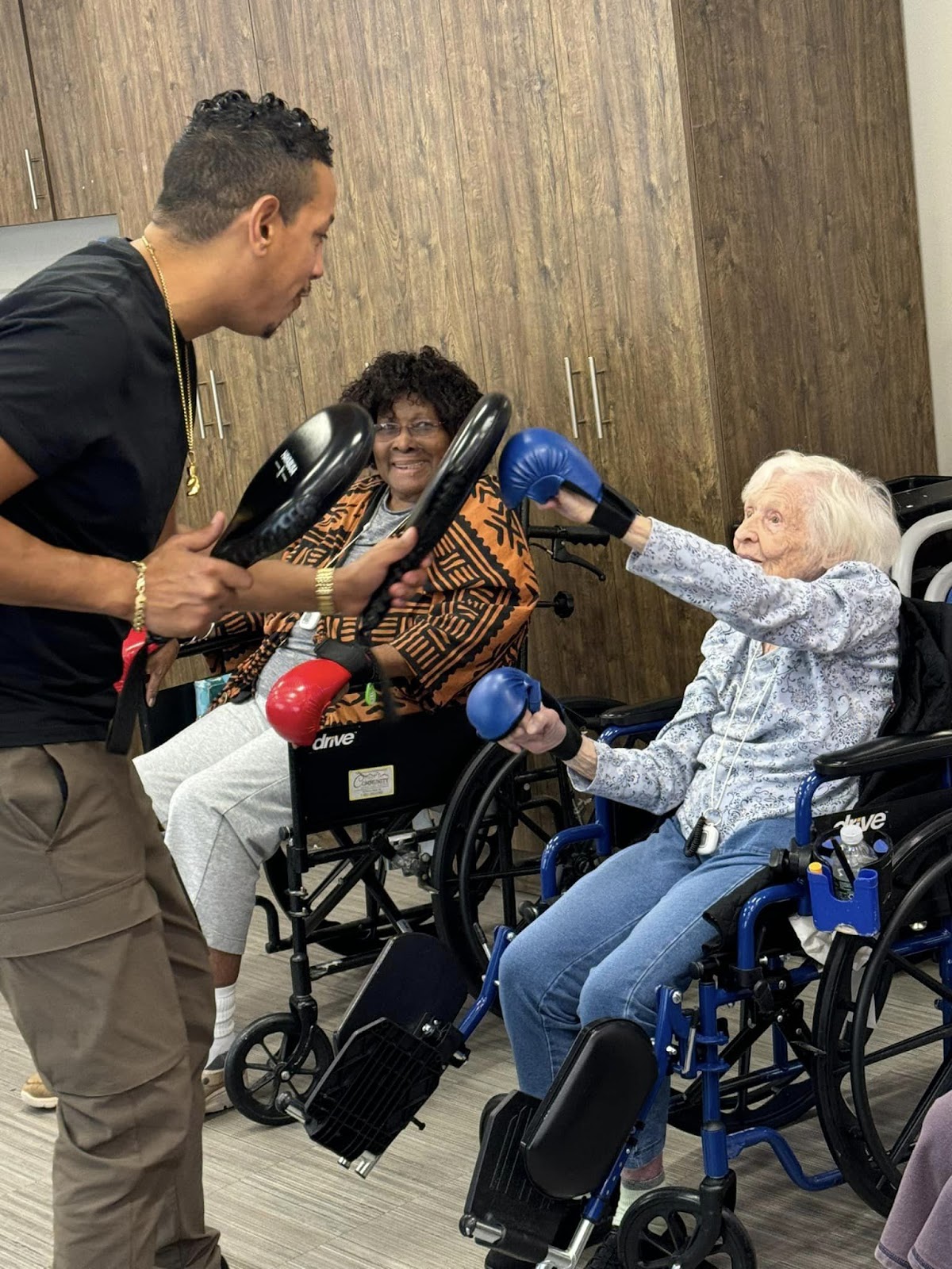 An elderly woman in a wheelchair lightly boxing with a person in a memory care activity