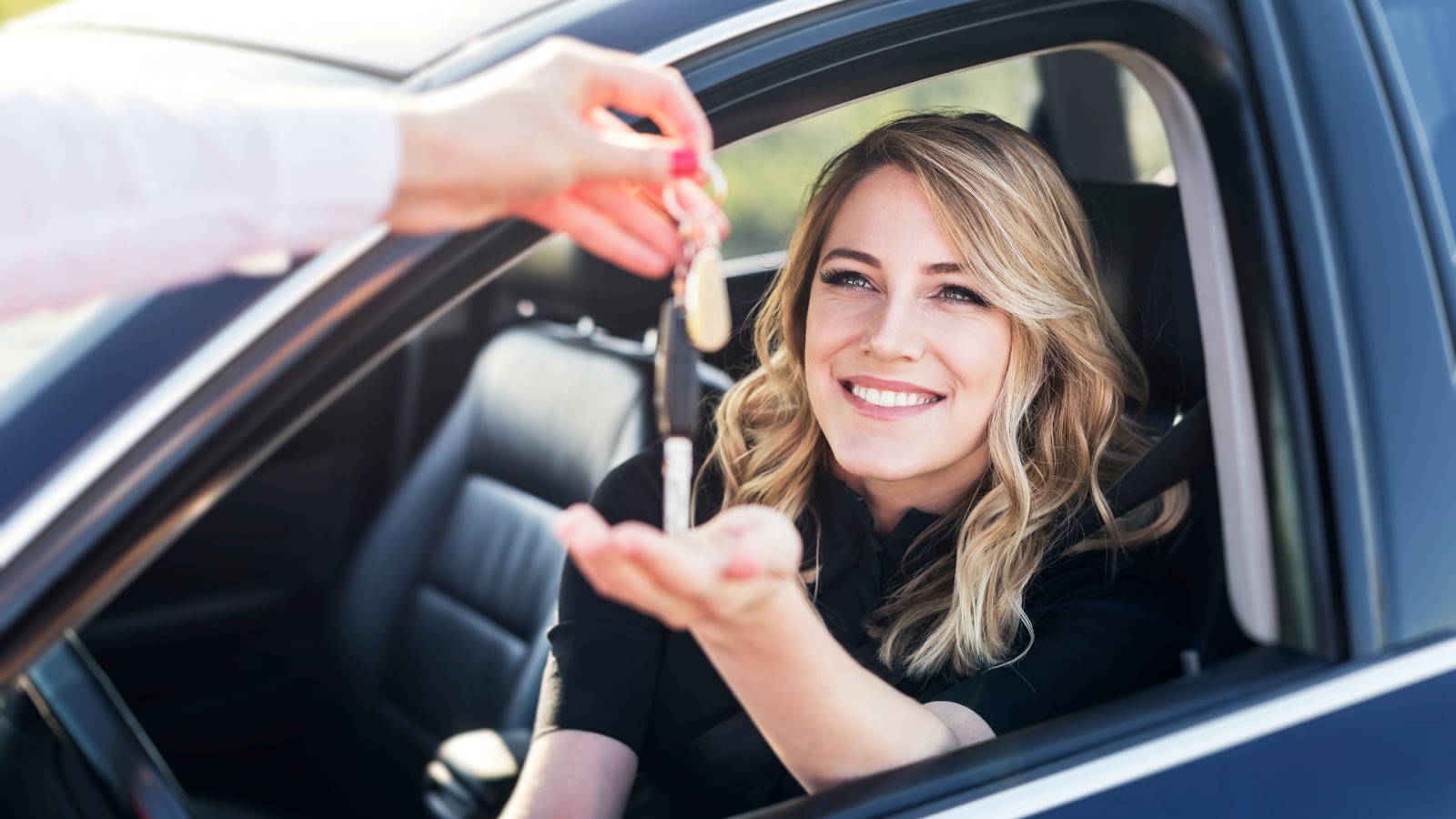 A woman inside her car smiles and reaches out to receive her duplicate car key.