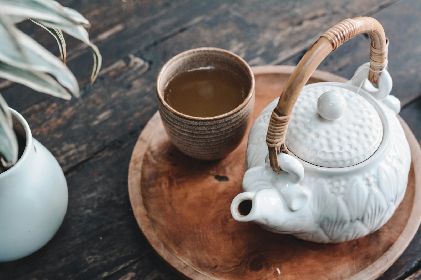 A wooden tray with a cup of tea, a saucer, and a spoon on it.