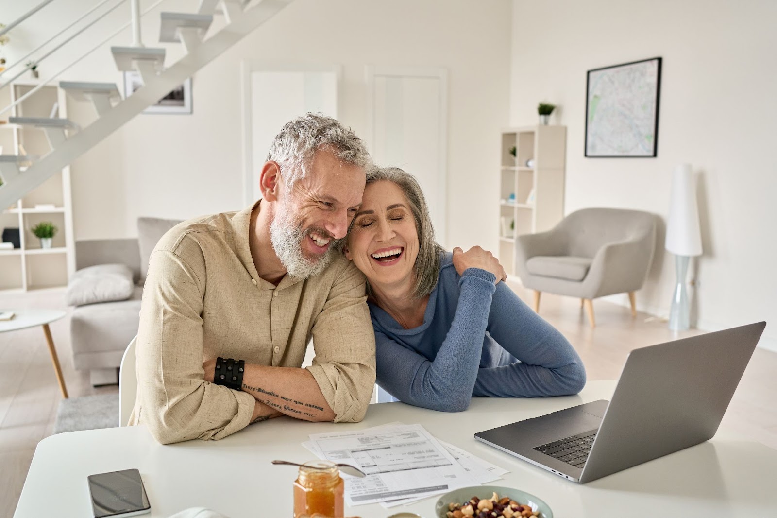 A happy middle-aged couple laughing at their computer in their home.