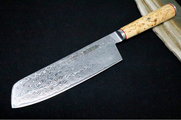 An image featuring the Miyabi Birchwood 6.5-inch Nakiri knife on a solid black and wood background.