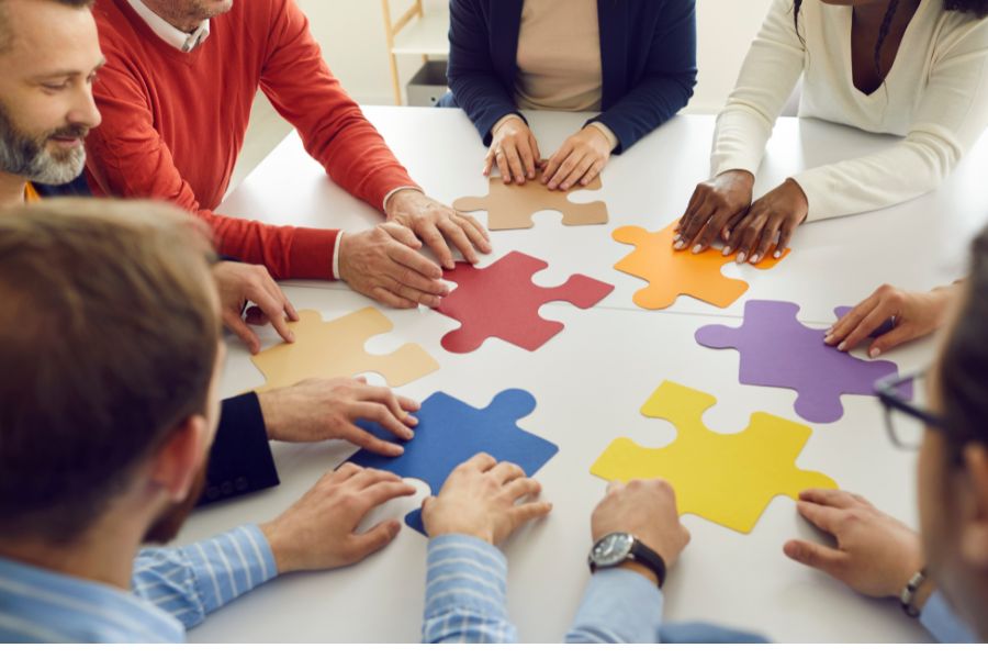 Group of people collaborating to assemble colorful puzzle pieces on a table.