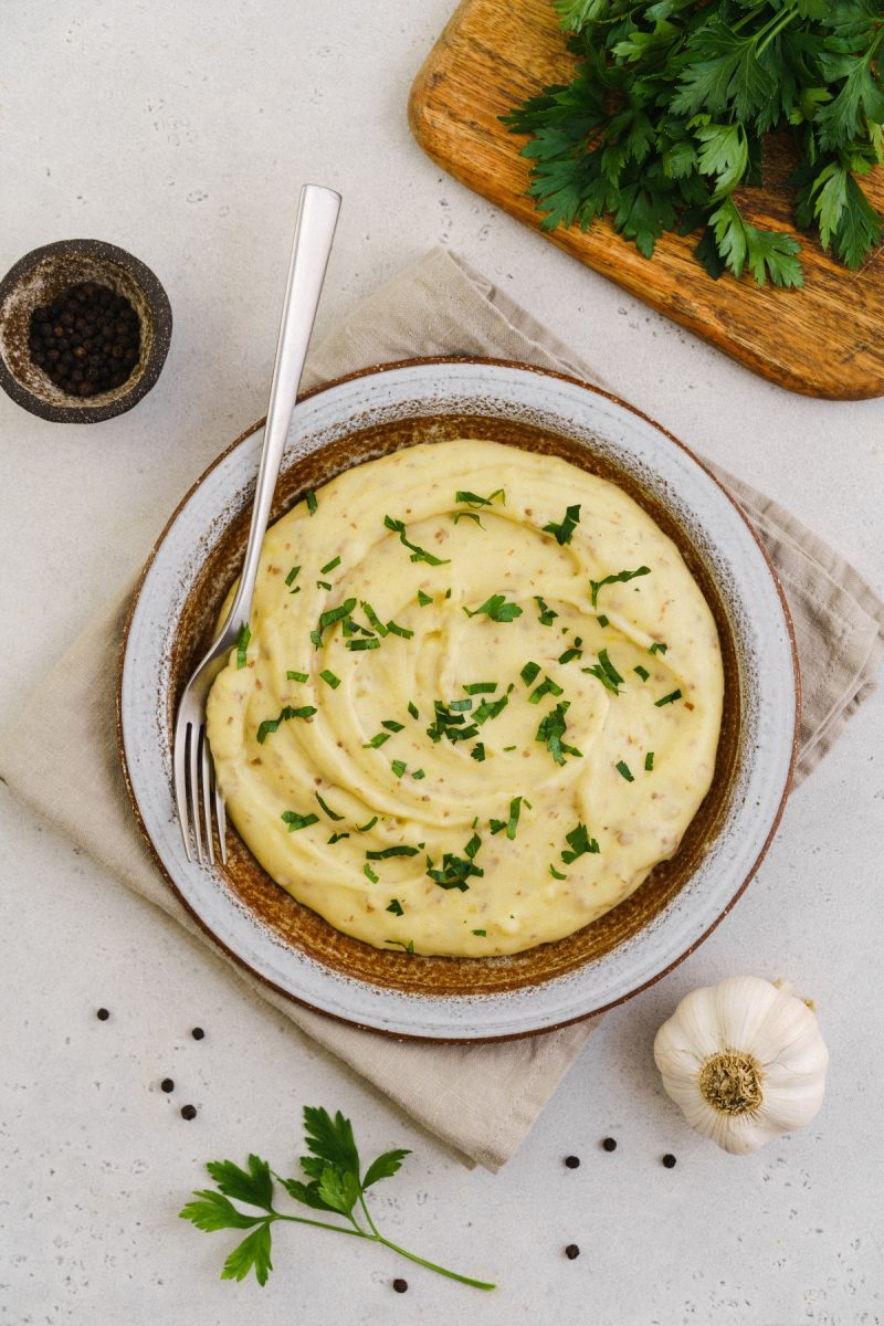 Red skin mashed potatoes on a plate with parsley and a fork.