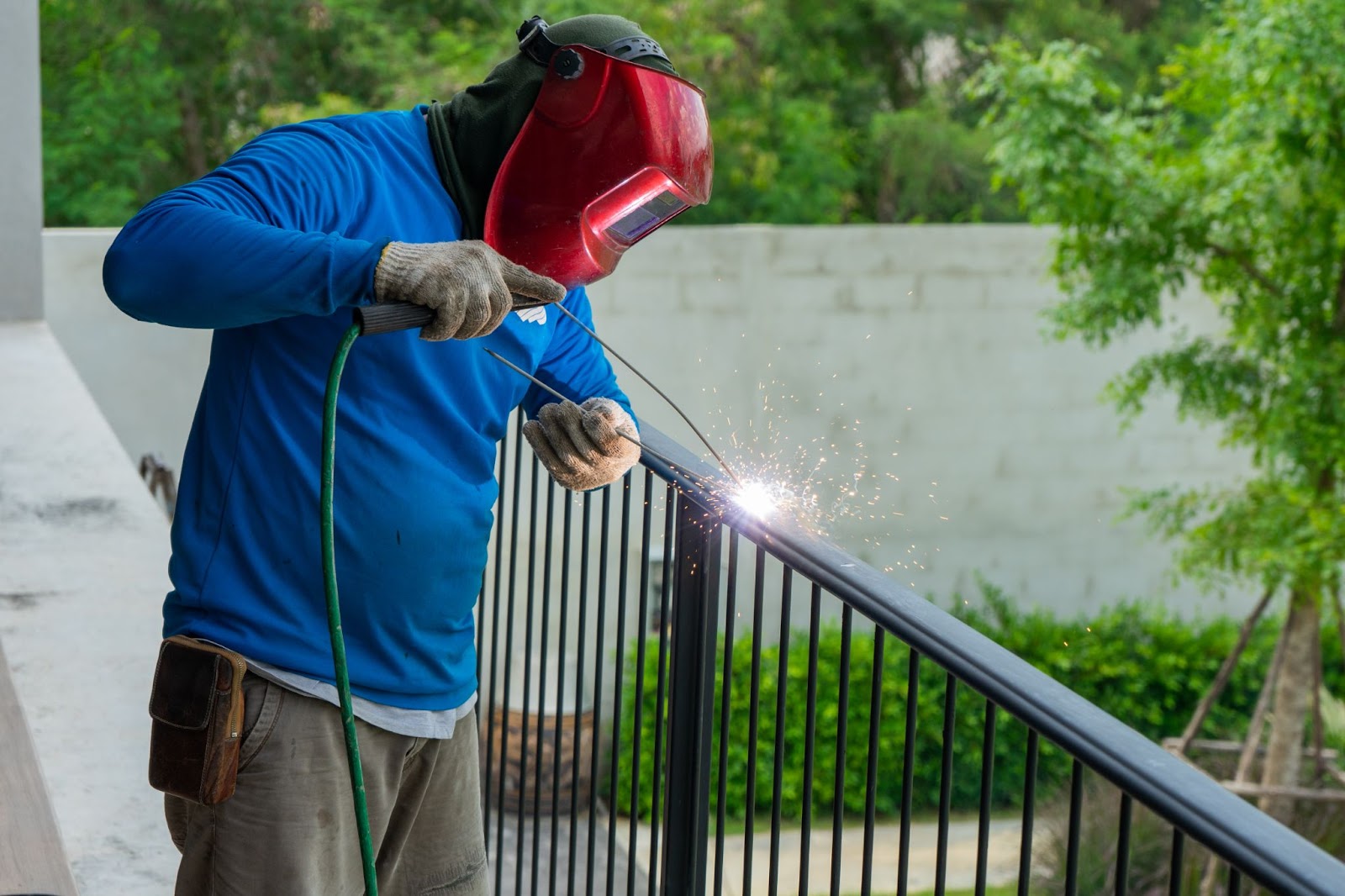 A male welder wearing a safety mask welds the steel fence.