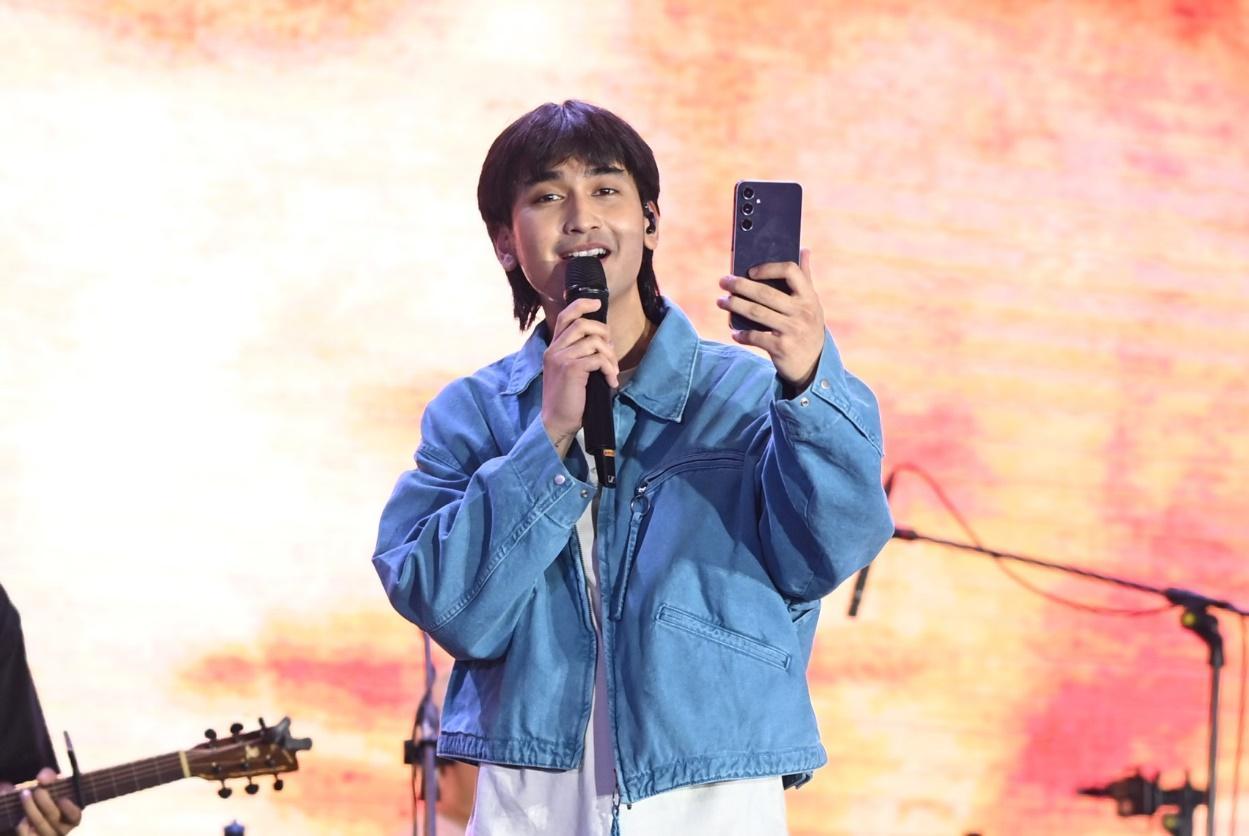 A person holding a phone and singing into a microphone
Description automatically generated