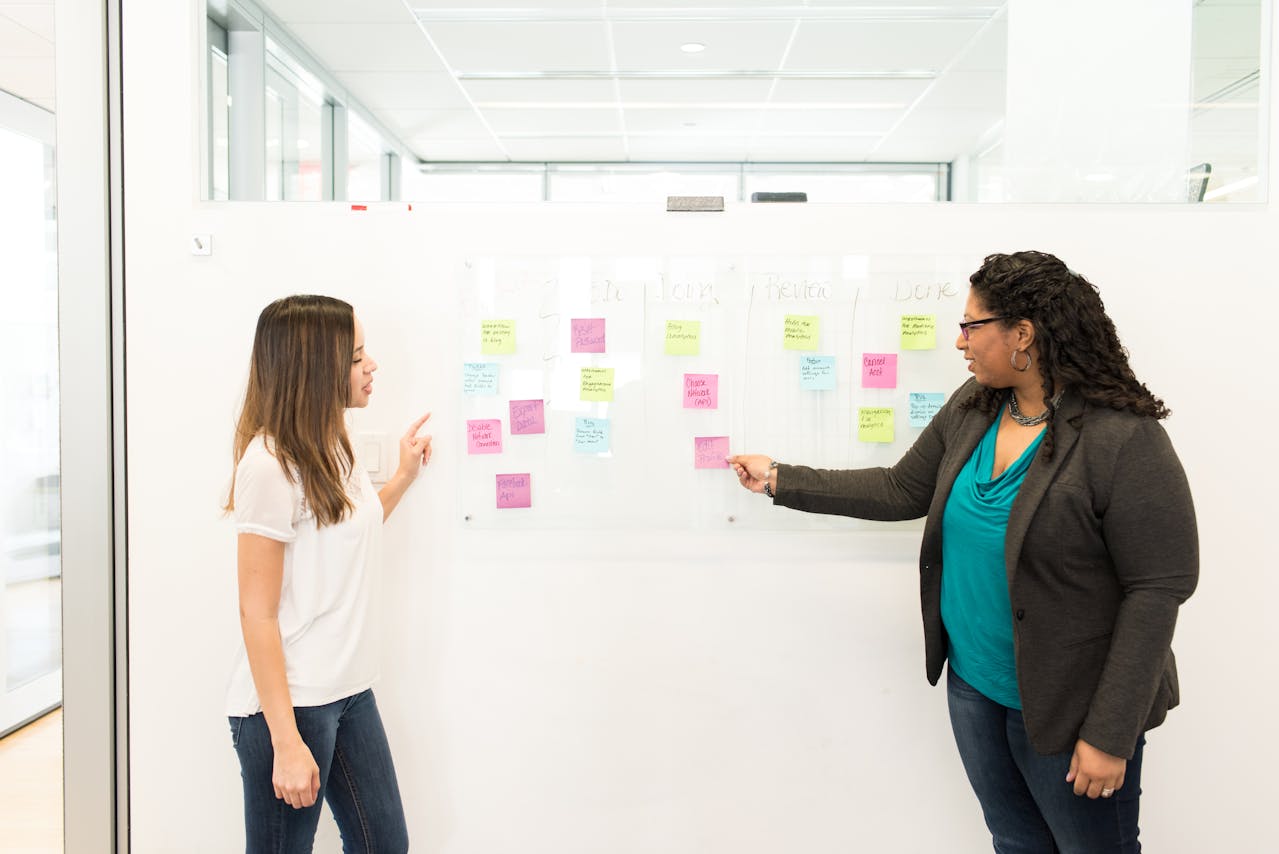 Two women presenting in front of a white board filled with sticky notes.