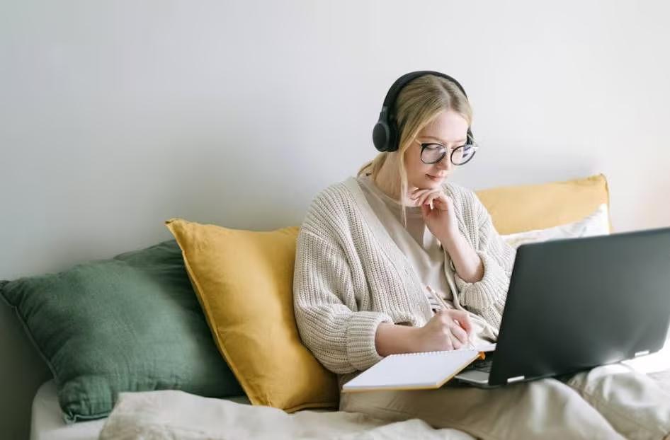 A person sitting on a bed with a computer and headphones

Description automatically generated