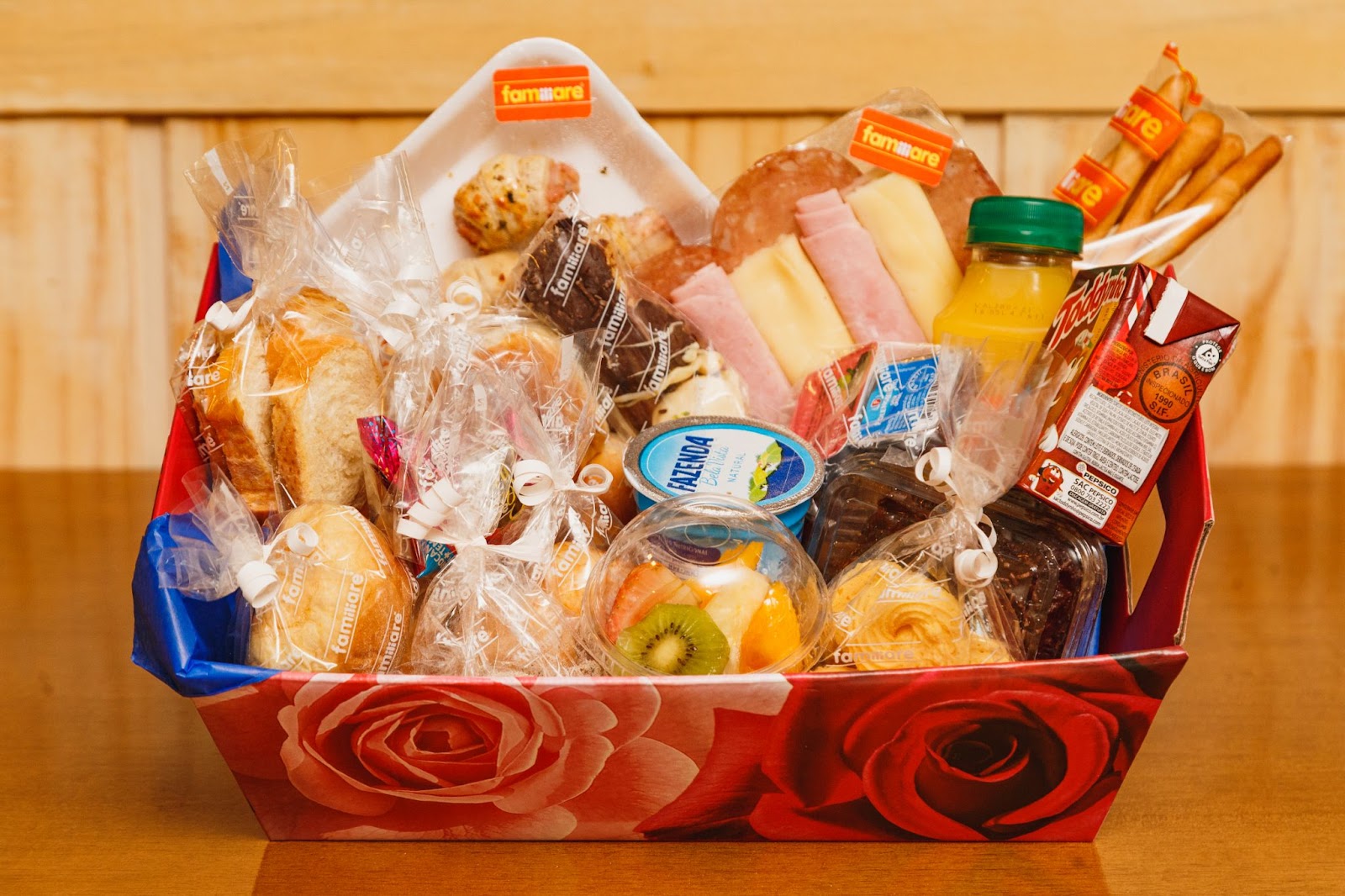 A colorful gift basket filled with various snacks including bread rolls, pastries, fruit slices, juice, chocolate milk, and packaged food items is perfect for sending packages in the mail.