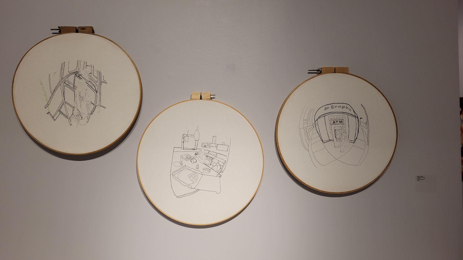 Image: Three pieces from Sabba S. Elahi’s drone stories series. The image is of three, black-and-white, monochromatic embroidery hoops with fisheye vignettes of daily life. The left hoop features a figure seated on the CTA; the middle hoop features two figures at a kitchen table in a home; the right hoop features a figure at an ATM on a corner. Photo by Saadia Pervaiz.