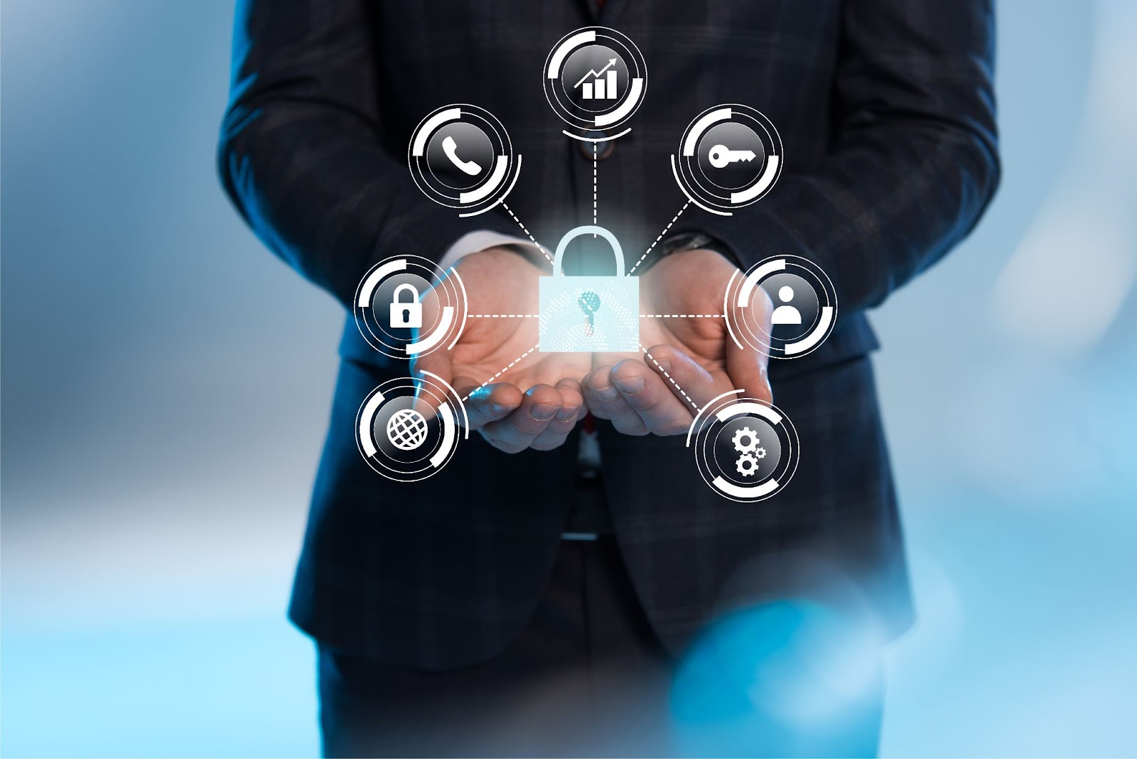 (A person in a suit holds a hologram of a padlock surrounded by various icons, including a phone, graph, key, shield, and user symbol, depicting cybersecurity and data protection—highlighting the importance of security in business.)