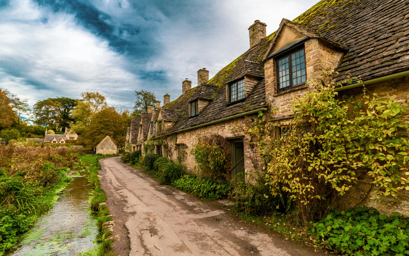 A row of stone buildings with trees and a roadDescription automatically generated