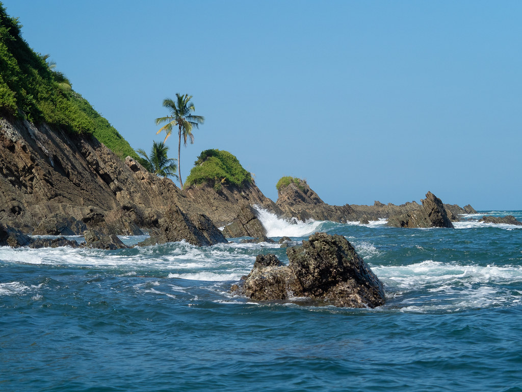 Gushing waves against majestic rocks and palm trees in one of the best beaches in Costa Rica