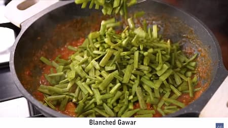Blanched gawar beans being added to the cooked tomato and masala mixture, with the pan covered for simmering.