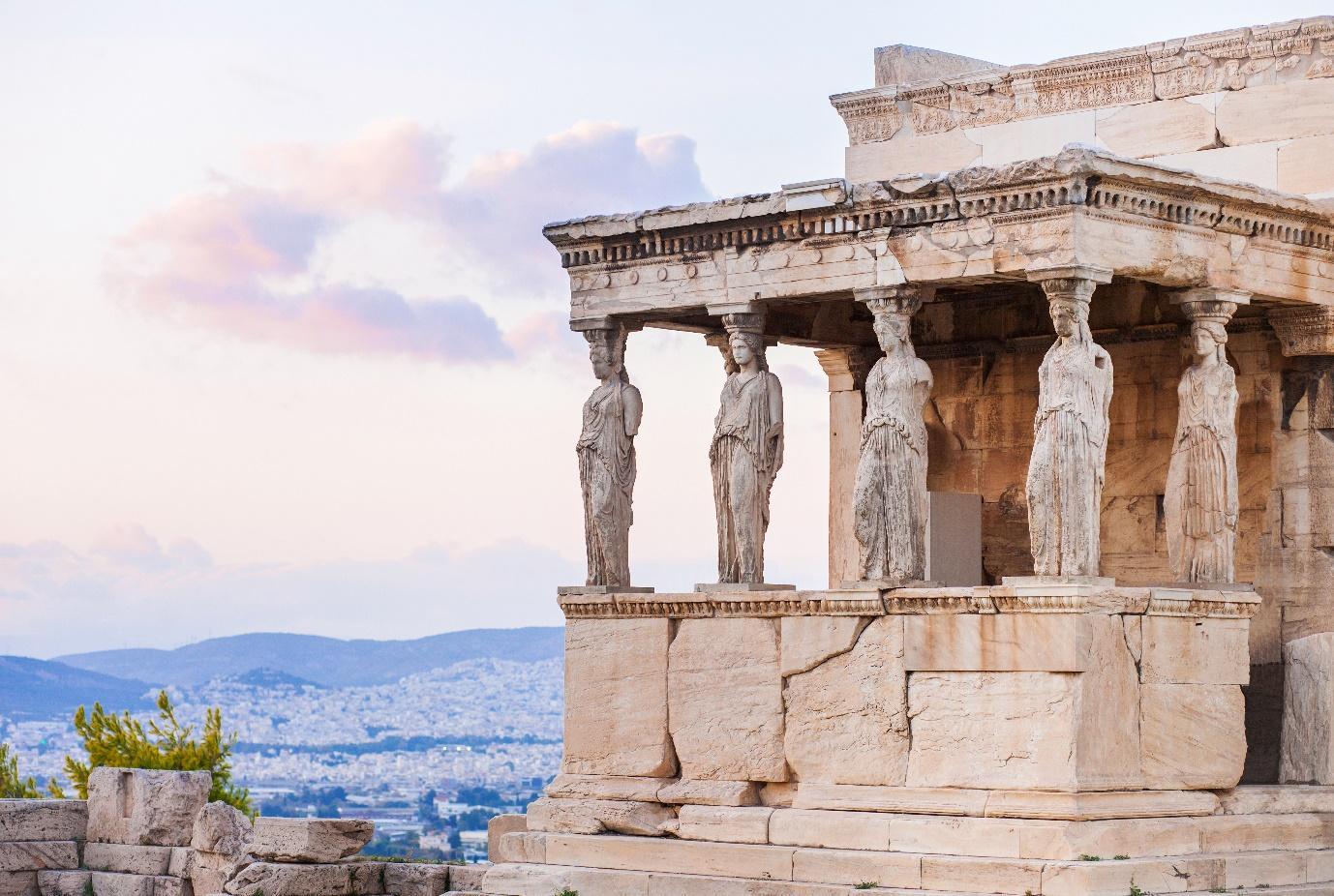 A stone structure with statues on the side with Erechtheion in the background

Description automatically generated