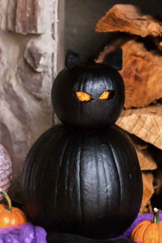 pumpkin carving ideas, two black pumpkins stacked on top of each other to look like a cat with carved out eyes