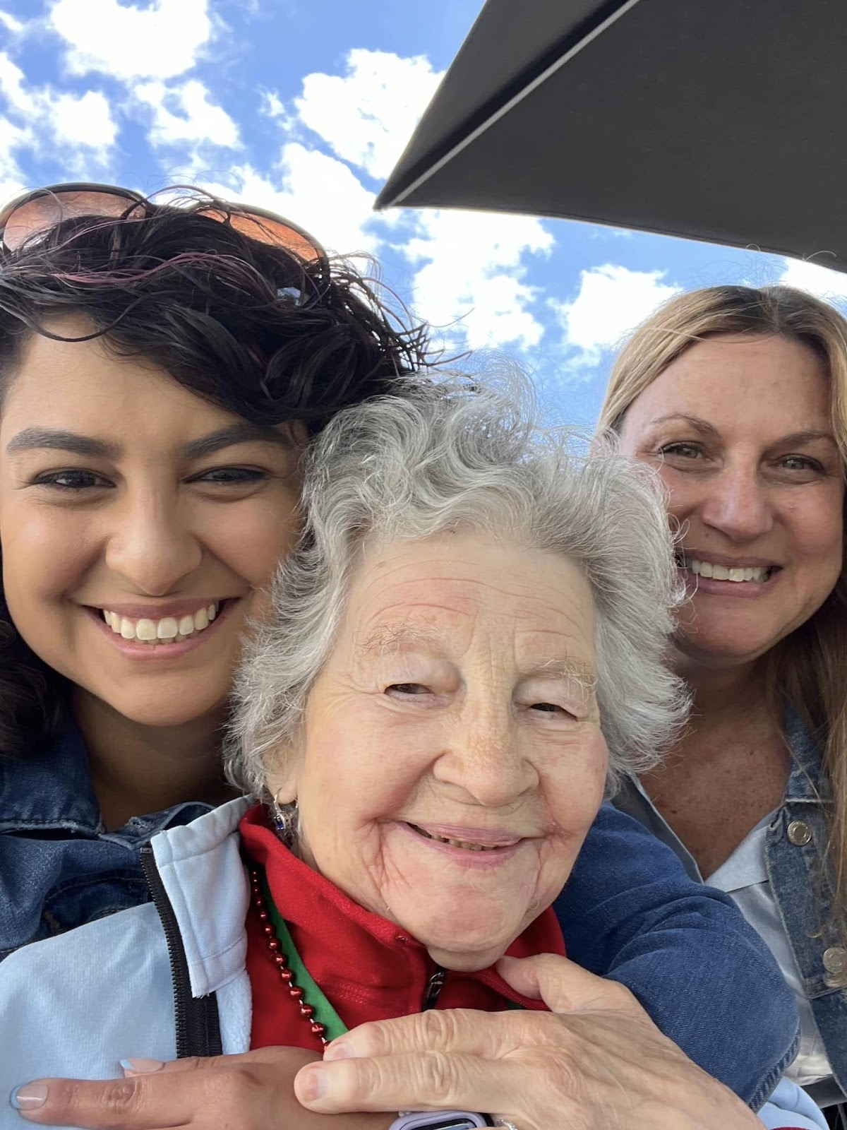 A senior citizen smiling with her caregivers — and presumably not feeling the cost of in-home dementia care