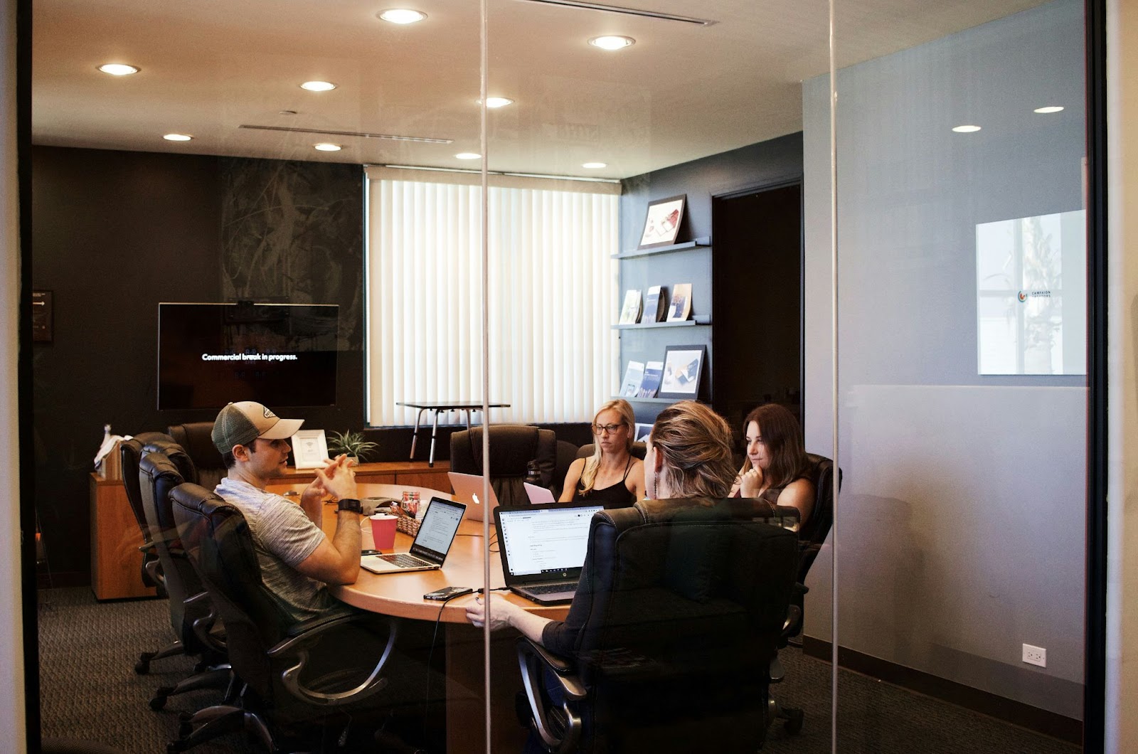A group of people sitting around a conference table with laptops, engaged in a discussion.