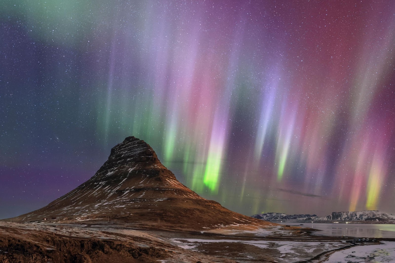 a night sky full of pink, purple and green colors from aurora borealis with a volcano in the foreground