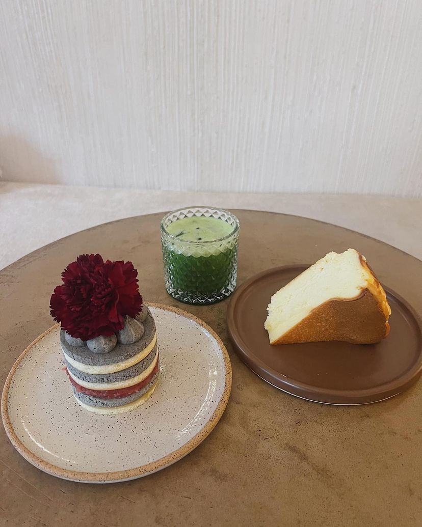 Small table with a matcha latte, slice of cake, and layered cake with decorative flower on top