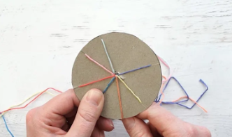 A person holding a circular piece of paper with colorful threads

Description automatically generated