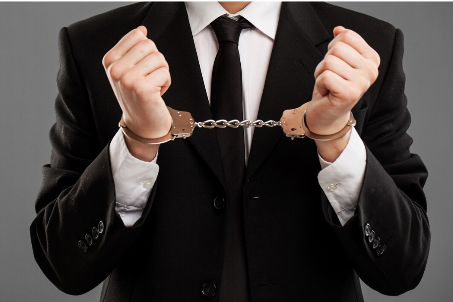 A businessman in a suit with handcuffs on, symbolizing white-collar crime